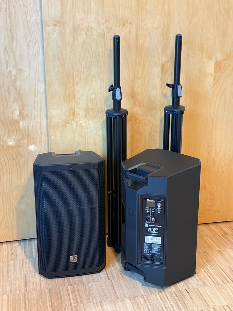 Two Electro-Voice ZLX 12P G2 speakers next to two folded tripod stands